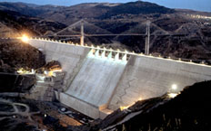 Vue aérienne nocturne de la partie centrale du barrage, avec un pont suspendu au pied du barrage
