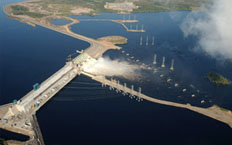 Vue aérienne du barrage hydroélectrique évacuant l'eau entouré de poteaux hydroélectriques chargés de transporter l'énergie